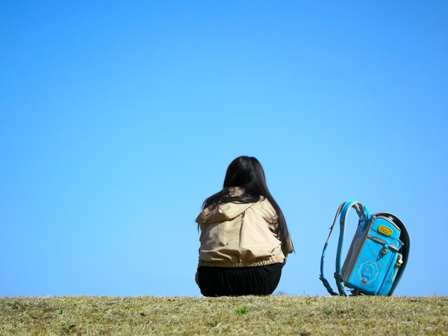 土手でランドセルを置いて空を眺める女の子